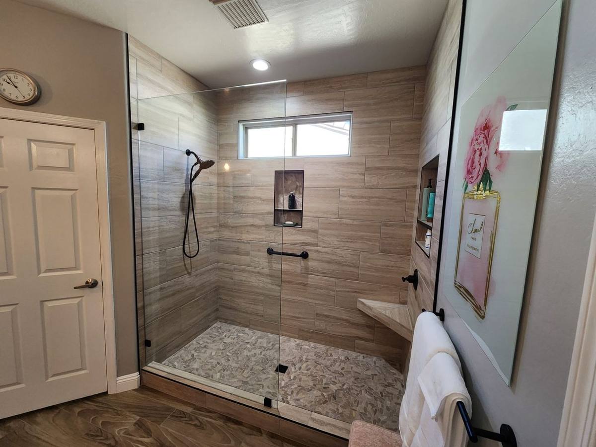 Modern walk-in shower with wood-look wall tile, pebble floor mosaic, and frameless glass enclosure