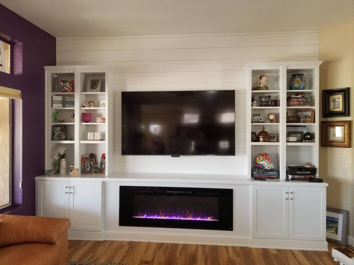 Custom white built-in cabinetry with an electric fireplace, shiplap wall, and wood flooring