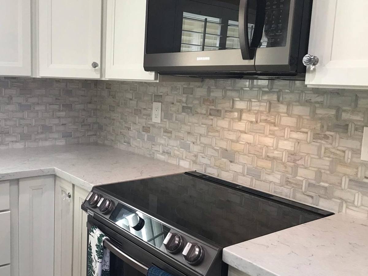 Natural stone mosaic tile backsplash behind a slide-in range with white shaker cabinets